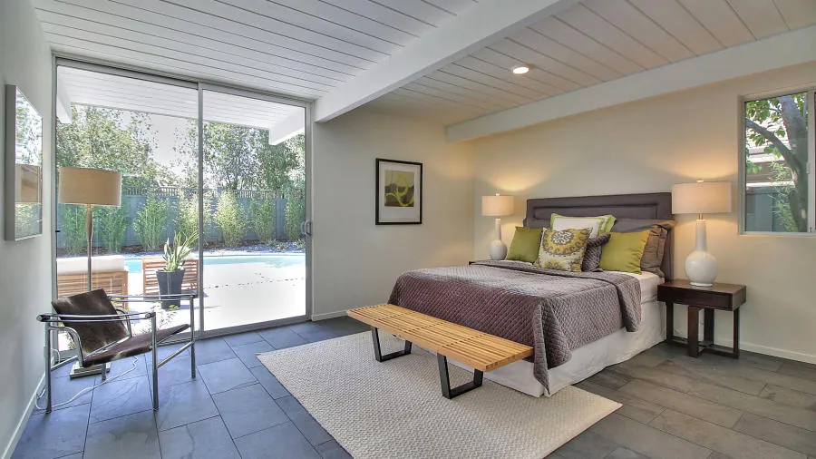 Bedroom at 1694 Clay Drive with exposed beams, a sliding glass door onto the pool terrace, and slate flooring continuous with the hall.