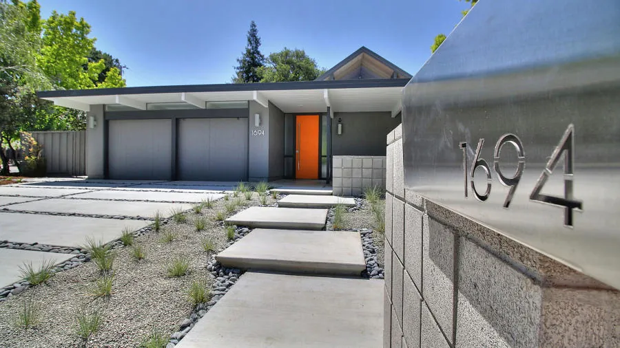 Entry at 1694 Clay Drive: an orange front door under a flat roof, flanked by a concrete block wall and screen-block panel, with the gable of the living room rising behind.