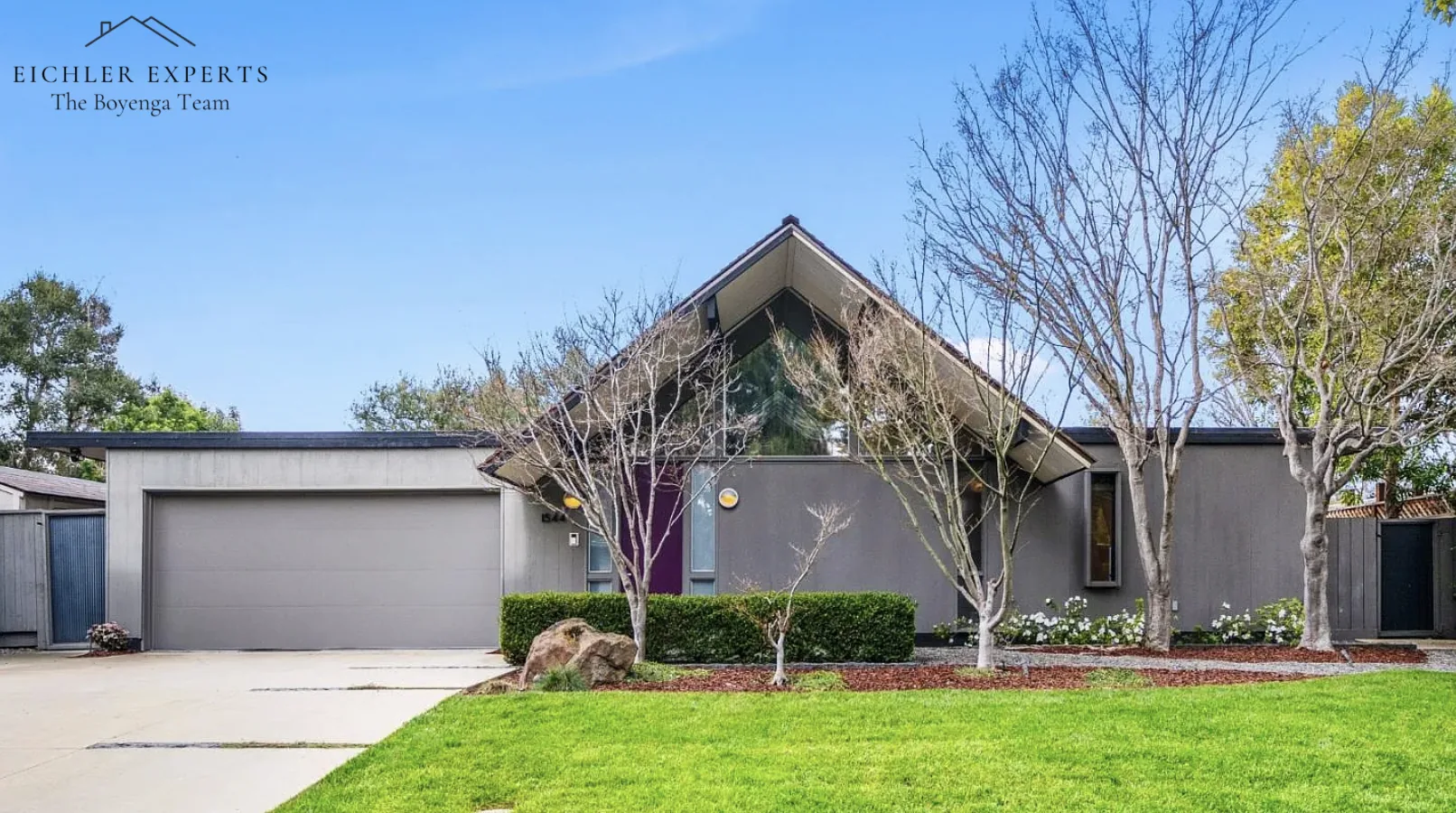 1544 Clay Drive, Los Altos: a gable-roofed Eichler with full-height clerestory glass under the ridge, grey stucco, magenta front door and a flat-roofed double garage pushed forward toward the street.