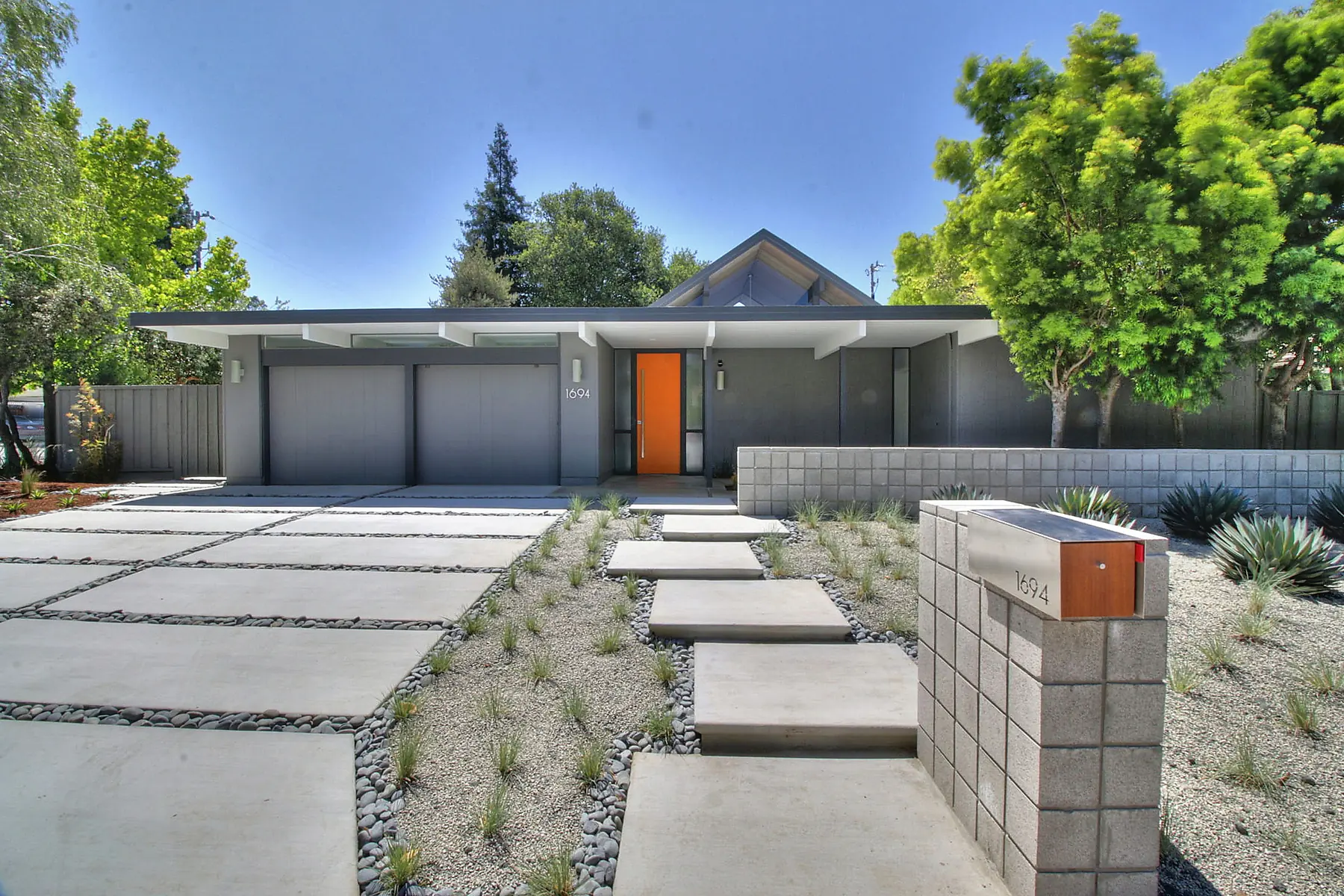 A restored Eichler on Clay Drive in the Fallen Leaf Park tract, Los Altos: flat and gable roofline, orange front door, concrete block wall and drought planting.